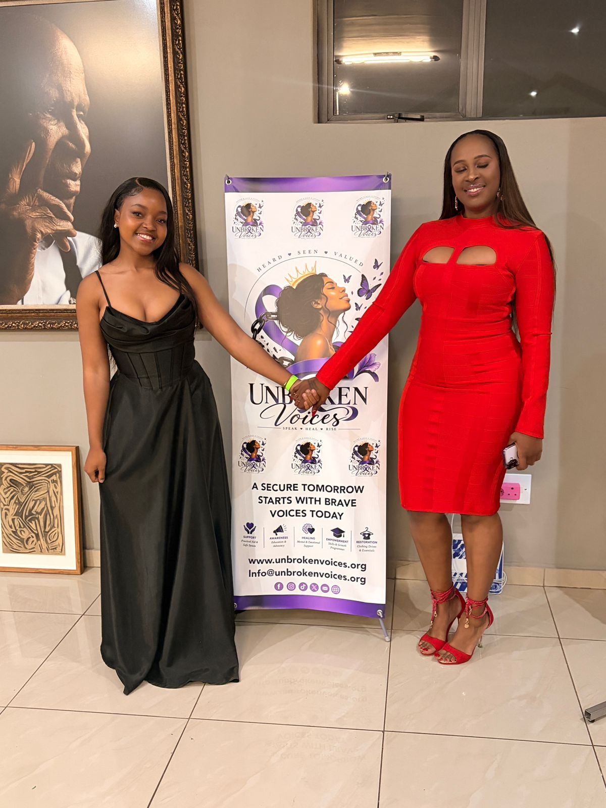 Two women holding hands beside an event banner